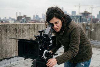 Jeune femme passionnée de cinéma filmant avec une caméra professionnelle sur un toit urbain, illustrant l'attrait des formations cinématographiques pour les jeunes talents